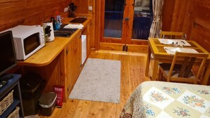 A compact wooden cabin with a kitchenette, a dining area, and a large sliding glass door leading to an outdoor deck.