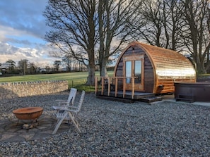 A rustic wooden cabin with a curved roof, a stone wall, a fire pit, and a wooden chair. - "The Pod" Fabulous glamping pod near Snowdonia.
(Pontllyfni)