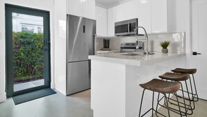 A modern kitchen with white cabinetry, stainless steel appliances, a built-in microwave, and a small island with stools. - Villa 3 in Miami (Miami)