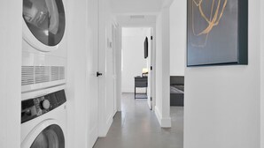 A laundry room with stacked washers and dryers, a hallway leading to a bedroom, and a framed abstract painting on the wall. - Villa 3 in Miami (Miami)