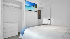 A bedroom with a bed, a wardrobe, a painting of a beach, and a door. - Villa 3 in Miami (Miami)