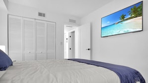 A bedroom with a bed, a TV on the wall, and a view of a beach through an open door. - Nice Villa in Miami 4 (Miami)
