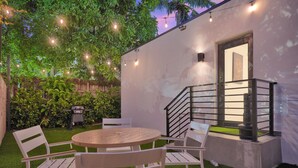 A patio with a round table and chairs, surrounded by lush greenery and string lights. - Nice Villa in Miami 4 (Miami)