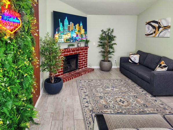 Een woonkamer met een schouw van baksteen, een groot schilderij van een stadshemelbeeld, een bank en een plant in pot.