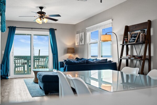 A living room with a glass table, blue sofa, and a ceiling fan.