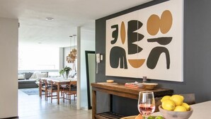 A modern kitchen with a dining area, featuring a wooden table with a fruit bowl and a wine glass.