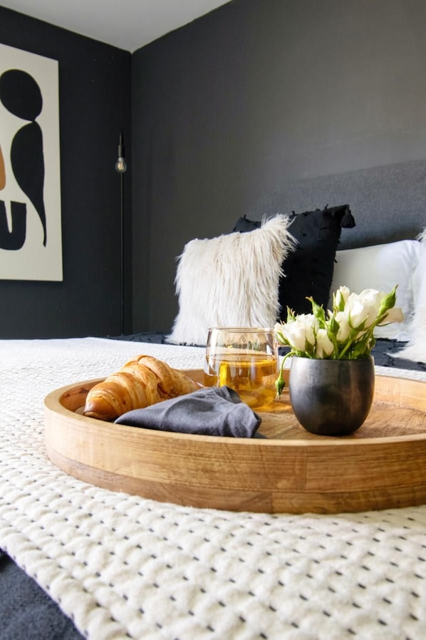A bedroom with a bed, a bedside table with a tray of food, a vase with flowers, and a wall art piece.