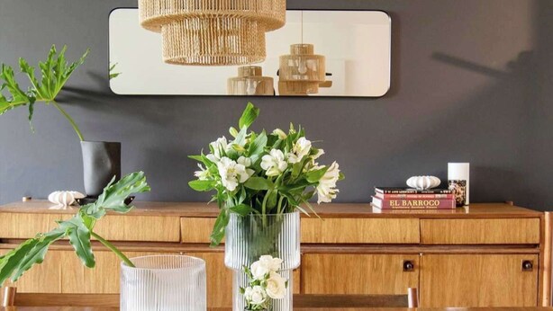 A modern interior with a wooden console table, a mirror, and three wicker pendant lights.