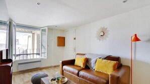 A living room with a brown leather sofa, a wooden coffee table, a red floor lamp, and a large window with a view of the outside. - Paris Marais Best WE MERRIS (Paris)