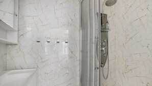A bathroom with a glass-enclosed shower, a white bathtub, and marble walls. - Paris Marais Best Trip (Paris)