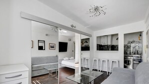 A modern, compact living space with a sofa, a glass coffee table, a mirrored wardrobe, a small kitchenette, and a washing machine. - Paris Marais Best Trip (Paris)