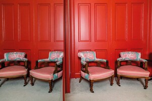A mirrored view of two antique-style chairs with floral upholstery and wooden frames, positioned in front of a red paneled wall.