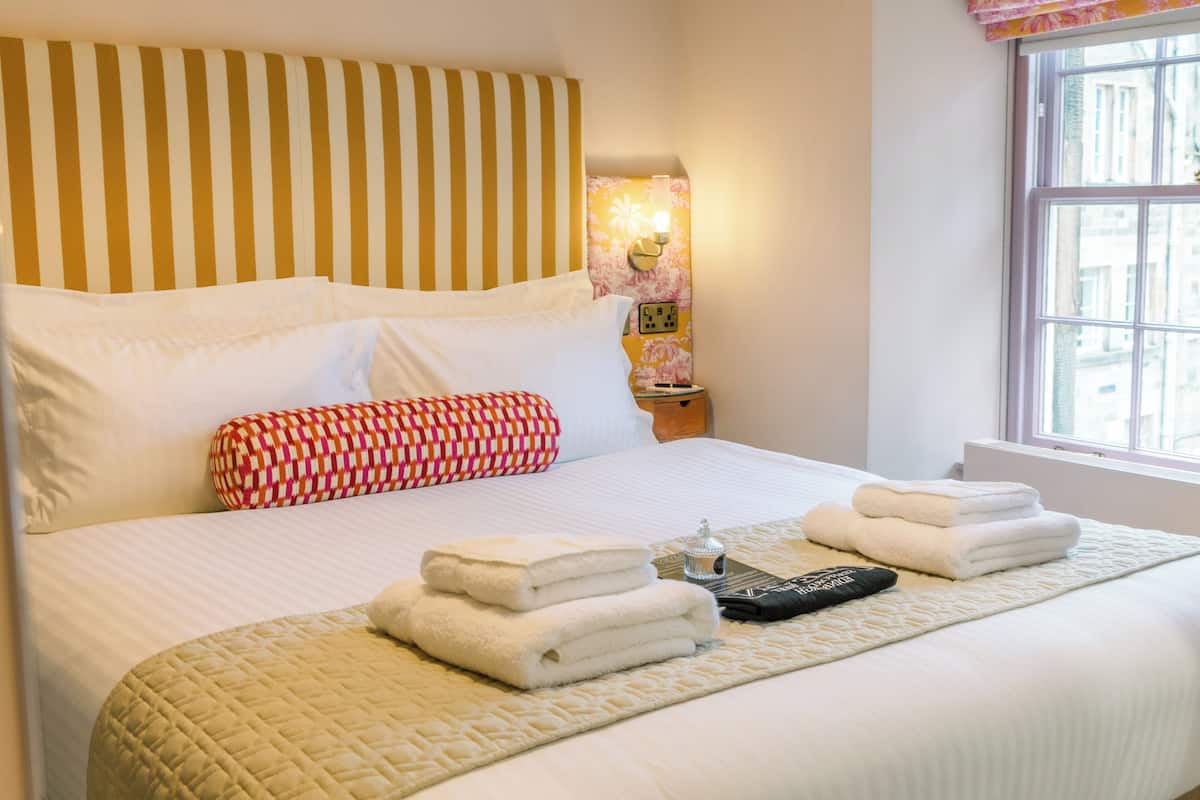 Een net opgemaakt bed met witte lakens, een gewatteerde plaid en een bedlampje.