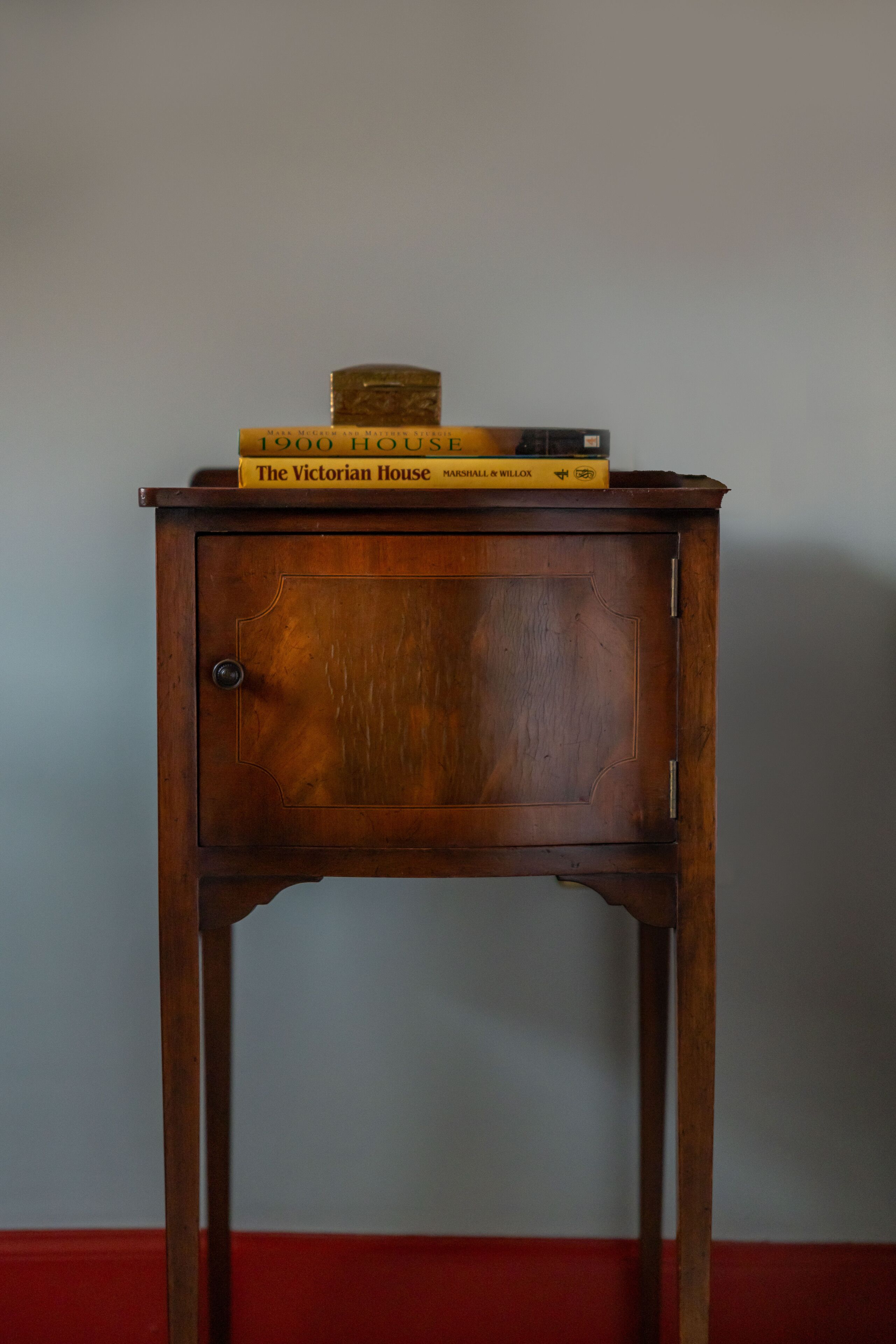 Een houten bijzettafeltje met een kastje en een stapel boeken erop.