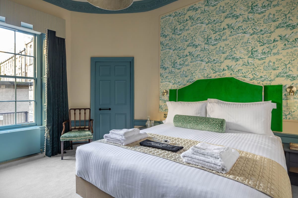 Een opgemaakt bed met witte lakens, een groen hoofdbord en een behang met een patroon.