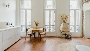 Una habitación con área de cocina, una mesa de comedor con sillas, un ventanal con vistas y un florero decorativo con flores.