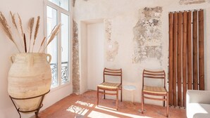 Una habitación con estética rústica, que incluye un jarrón grande, dos sillas de madera, una mesita redonda y una ventana con vistas al exterior.