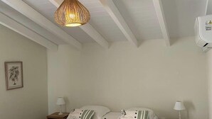 Une chambre à coucher comprenant un lit, des tables de chevet, un luminaire suspendu et un climatiseur fixé au mur.