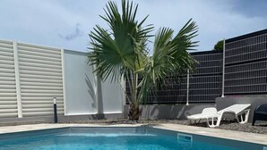 Une piscine d’un bleu éclatant, avec un palmier et des chaises longues.