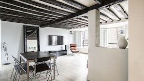 Un intérieur moderne comprenant un coin repas, un téléviseur fixé au mur et une grande fenêtre laissant entrer la lumière naturelle.