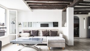 Un salon moderne avec une table basse à plateau de verre, un canapé gris agrémenté de coussins et des poutres apparentes en bois au plafond.