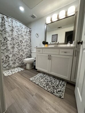 A bathroom with a toilet, sink, mirror, and vanity.