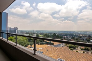 Un balcon doté d’une rambarde en métal, d’où l’on peut admirer un paysage urbain avec ses bâtiments et sa végétation.