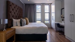 A modern hotel room with a large bed, a desk, and a view of the city. - Sandton Smart Apartment Seventeen (Sandton)