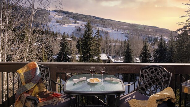 A balcony with a table set for two, overlooking a snowy landscape with trees and houses. - Walk to Chair 6 + Mountain Views | Chalet Crevasse (Vail)
