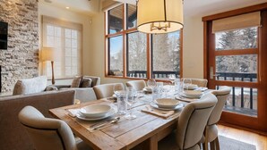 A dining area with a wooden table set for six, large windows, and a stone wall. - Vail Village Charm + Walk to Lifts| Chalet Schuss (Vail)