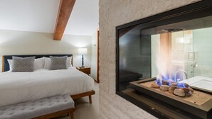 A bedroom with a bed, bedside table, lamp, and a fireplace with burning logs. - Vail Village Charm + Walk to Lifts| Chalet Schuss (Vail)