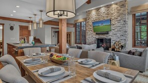 A spacious living area with a stone fireplace, a television mounted on the wall, and a dining table set for four.