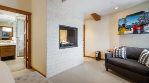A modern living room with a fireplace, a sofa with patterned cushions, and a painting of skiers on the wall.