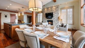 A modern kitchen with a stone accent wall, a dining area with a wooden table set for six, and a cozy living space with a fireplace. - Vail Village Charm + Walk to Lifts| Chalet Schuss (Vail)