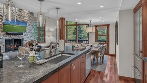 A modern kitchen with a stone wall, a fireplace, and a large window overlooking greenery.
