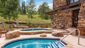 Um edifício de pedra com área de piscina, incluindo duas banheiras de hidromassagem e um espaço de estar com cadeiras e uma mesa.