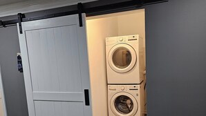 A compact laundry room with a front-loading washer and dryer, a sliding door, and a wooden floor. - Boxcar Bunker - Downtown living at its finest
 (Holly)