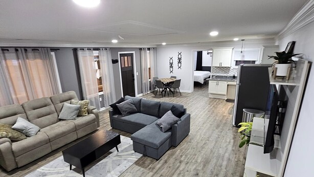 A modern living room with a grey sofa, a grey sectional, and a coffee table. There is a dining area with a table and chairs, and a kitchen with white cabinets and a black refrigerator. - Boxcar Bunker - Downtown living at its finest
 (Holly)