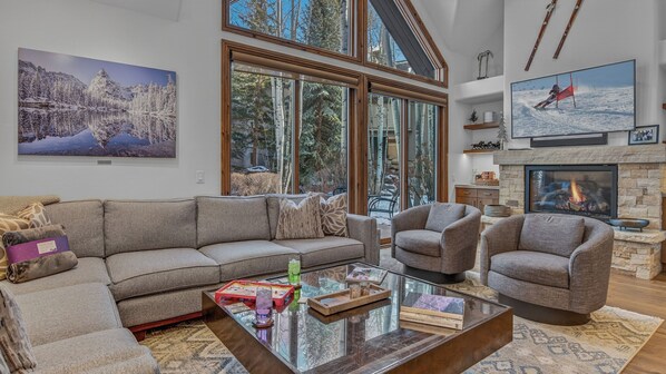 A spacious living room with a large window, a fireplace, and a cozy seating area. - Walk to Arrow Bahn Express | Icegrass Chalet (Edwards)