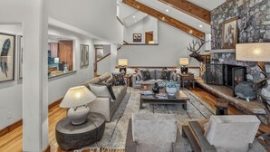 A spacious living room with a fireplace, a stone wall, and a high ceiling with exposed beams. - Firepit, Hot Tub + All the Views | Navigator Lodge (Avon)