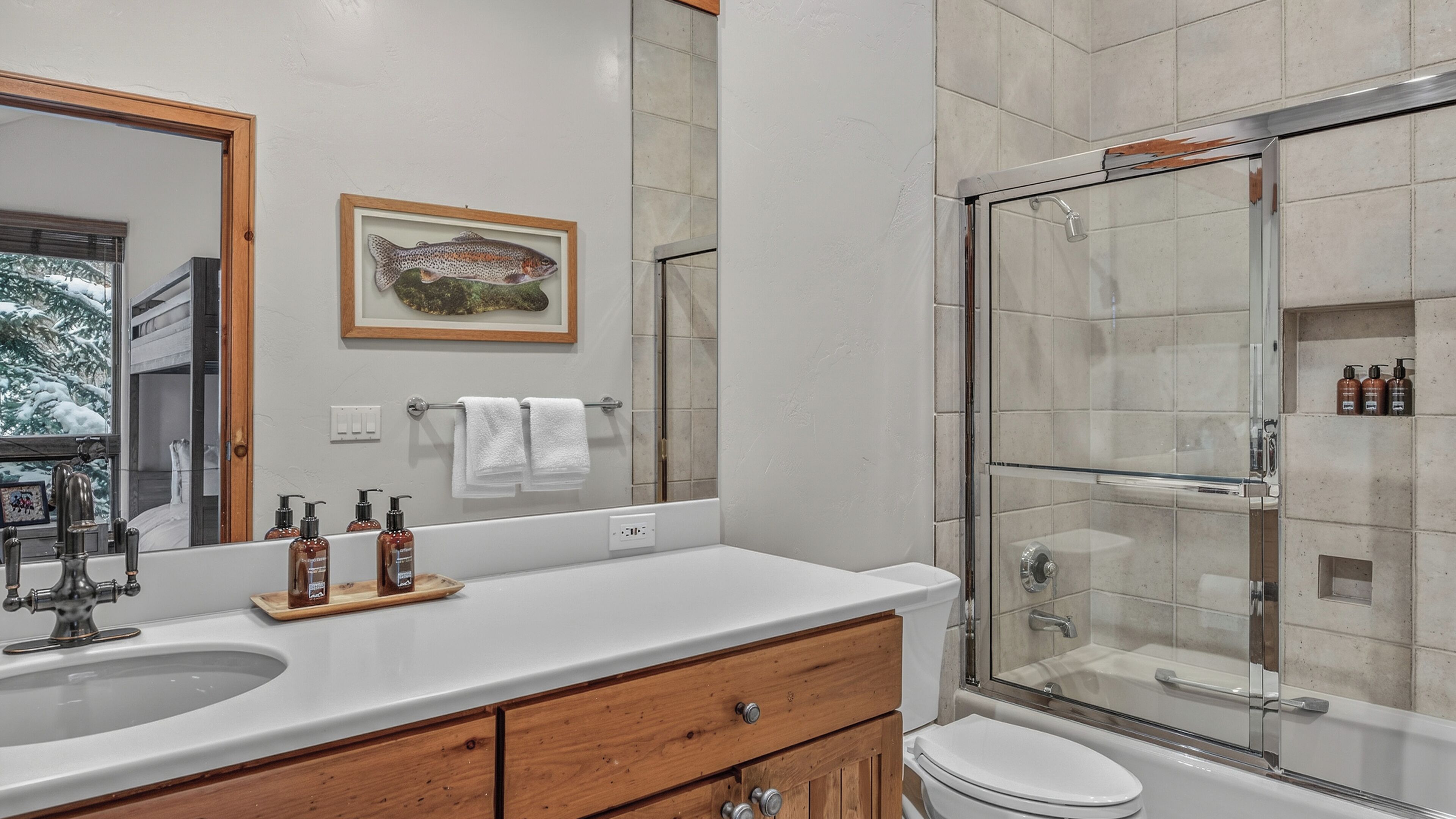 A bathroom with a double sink, a toilet, a glass shower enclosure, and a framed fish artwork on the wall.
