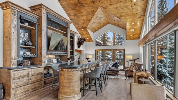 A spacious kitchen with a high ceiling, wooden beams, and large windows offering a view of snow-covered trees. - Firepit, Hot Tub + All the Views | Navigator Lodge (Avon)