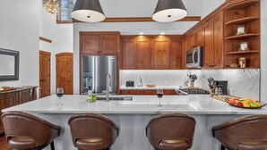 Een moderne keuken met houten kastjes, een roestvrijstalen koelkast, een groot eiland met barstoelen en een backsplash van visgraatmozaïek.