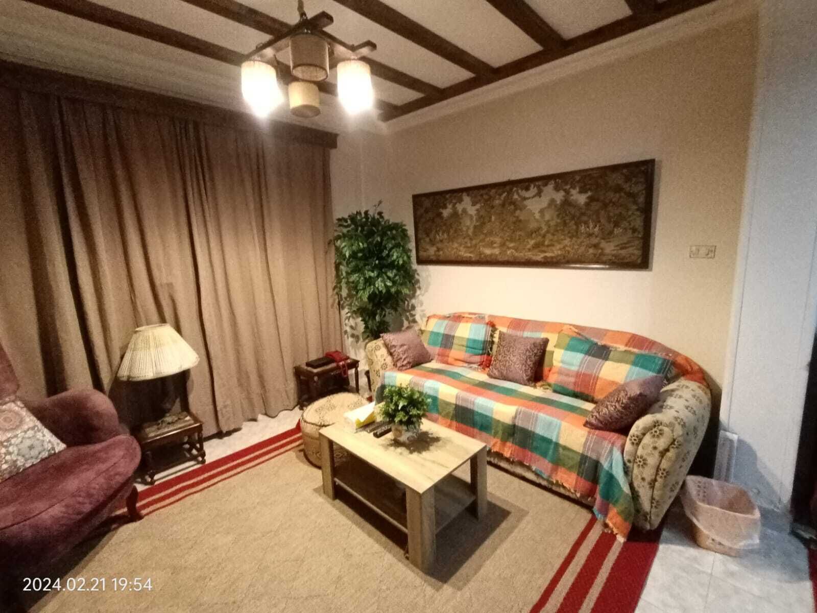 A cozy living room with a plaid sofa, a wooden coffee table, a red and white striped rug, a lamp, and a large painting on the wall.