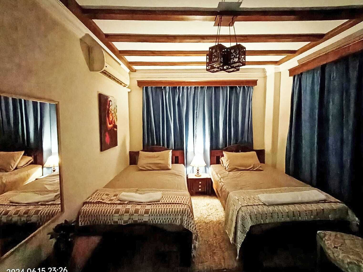 Une chambre avec deux lits, un luminaire suspendu et une fenêtre avec des rideaux.