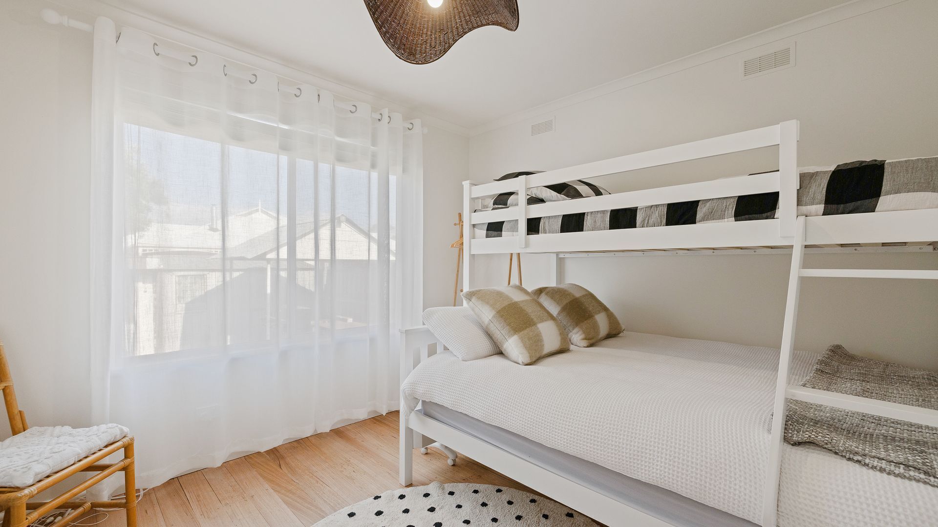 A bunk bed room with a window, a chair, and a woven floor lamp.