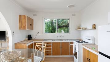 A compact kitchen with wooden cabinets, a white refrigerator, a stove, and a large window offering a view of greenery.