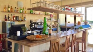 Un área de bar moderna con una barra alargada, sillas de madera y estantes llenos de botellas y vasos.