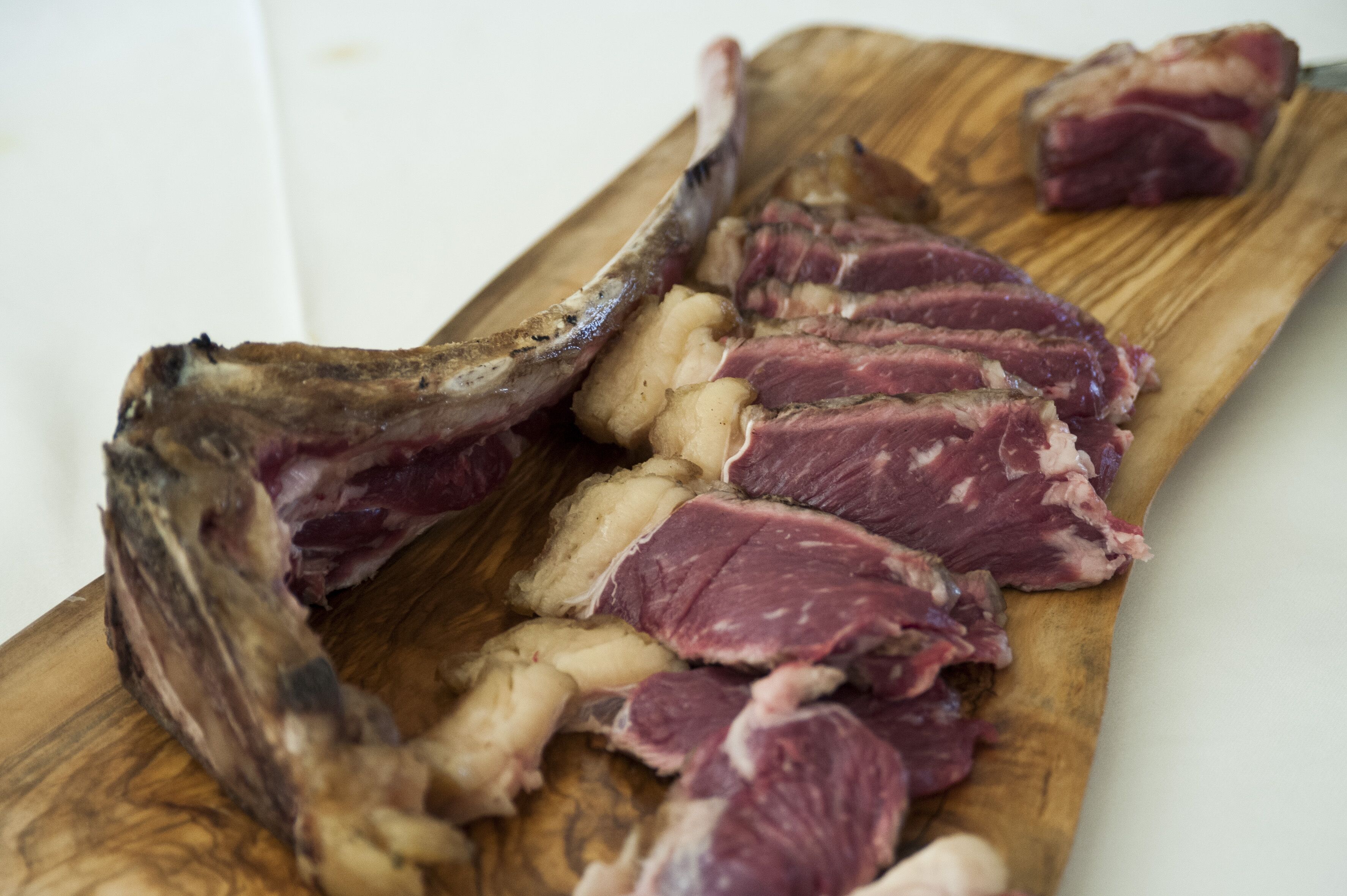 Une planche à découper en bois sur laquelle sont disposés un jarret d’agneau cuit et des côtes.