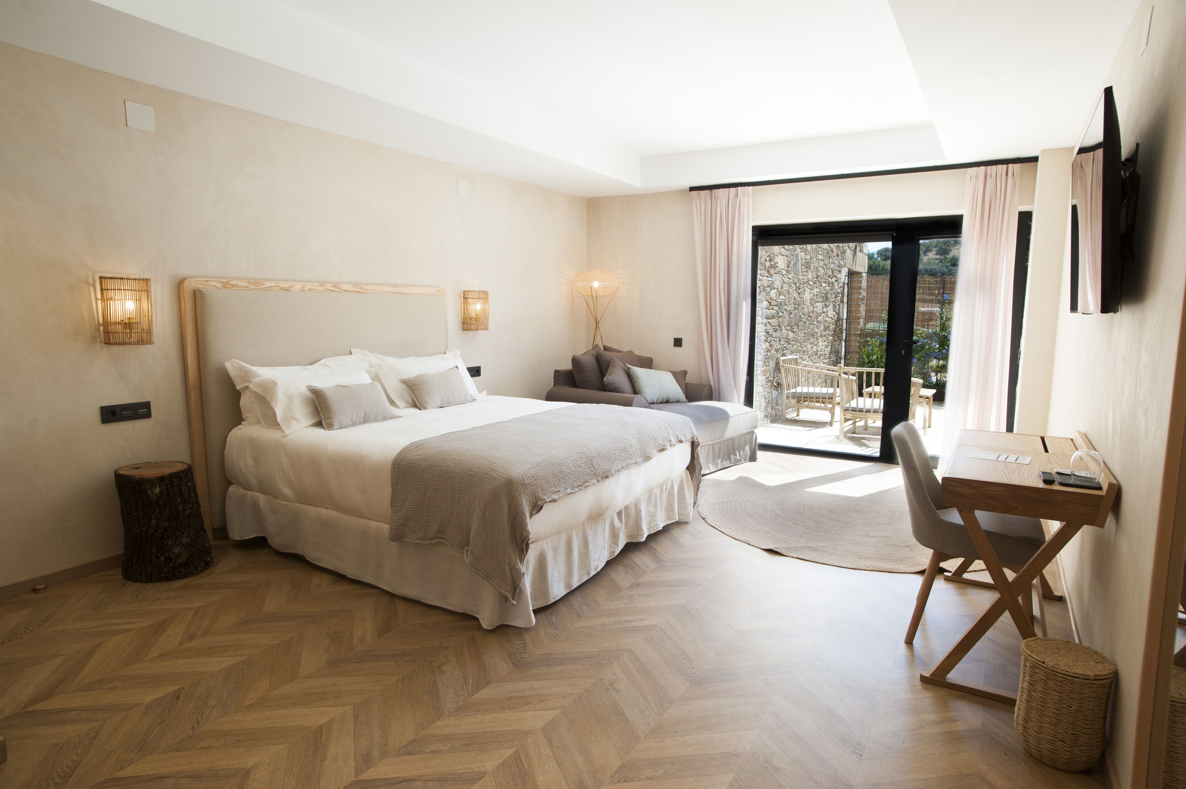 A bedroom with a large bed, a desk, and a view of the outdoors.